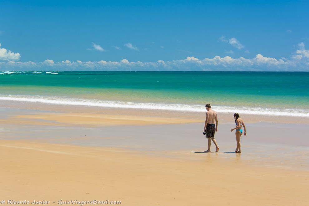 Imagem de casal andando nas areias molhadas da Praia Taipu de Fora.